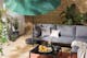 Outdoor-Loungesofa mit grauen Polstern, Kissen und Plaid, dazu ein schwarzer Tisch, Outdoor-Teppich und Grünpflanzen