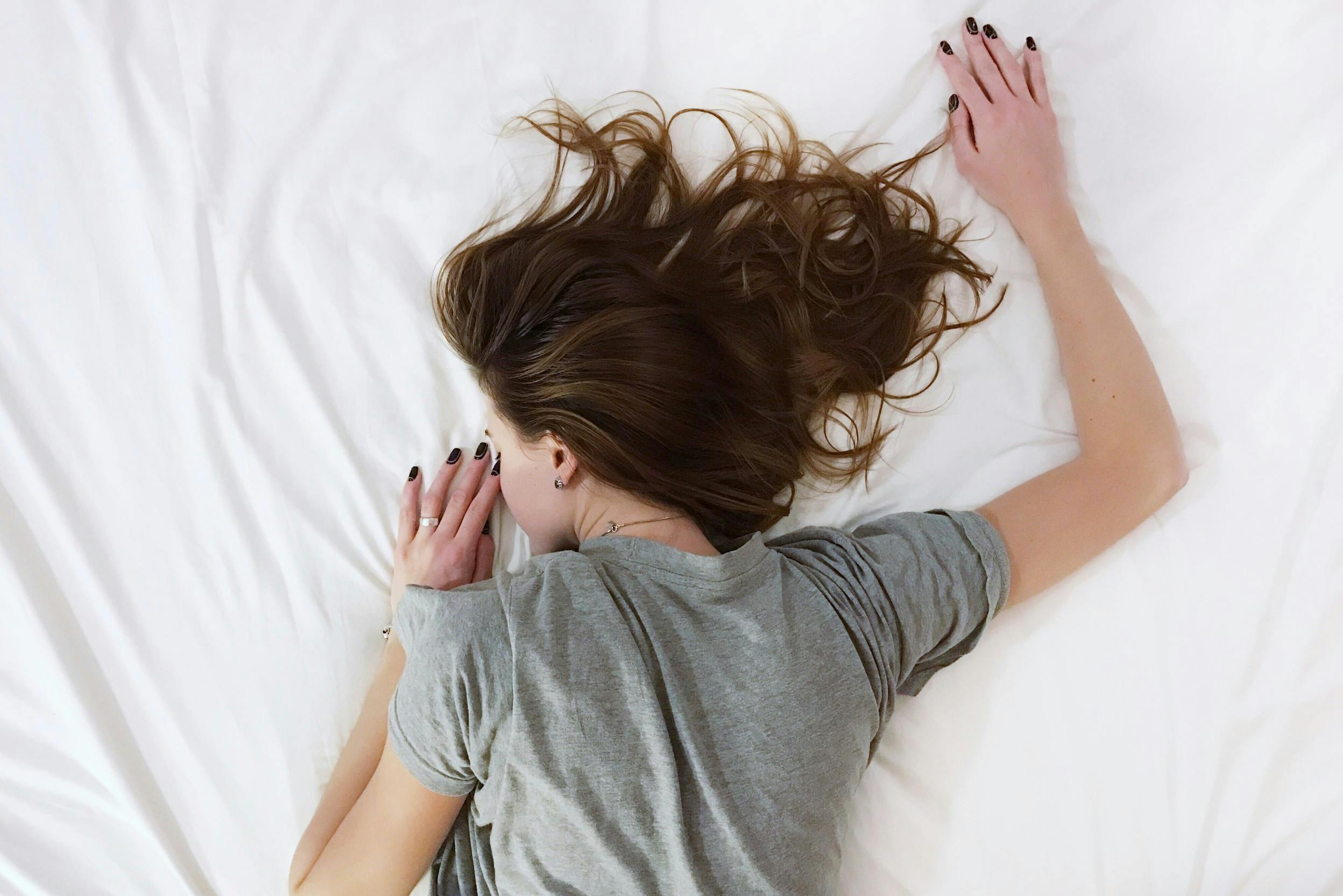 Frau in Bauchlage auf dem Bett mit ausgestrecktem Arm