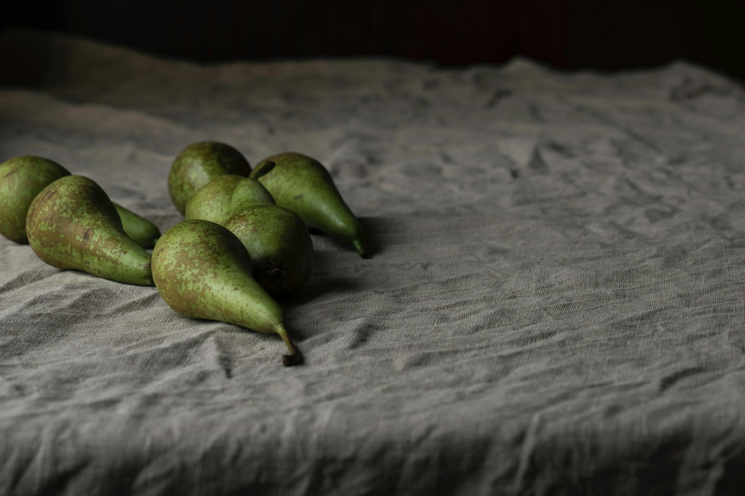 Bett mit Bettwäsche in Grau und grüne Birnen drauf (links). Bild: Joanna Kosinska, aus Unsplash
