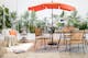 Terrasse de style bohème avec chaise suspendue, photophores en bambou, tapis d'extérieur noir et blanc et parasol orange, le tout accompagné de coussins et de plaids, de nombreuses plantes vertes et de meubles de jardin en acacia et en métal.