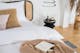 Zwart bed met Weens vlechtwerk, wit beddengoed, een beige kussen met franje, een beige gebreide deken, een zwart nachtkastje, plus een zwarte hanglamp en een vaas met pampagras.