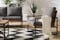 Terrazzo con divani modulari e tavolino in legno e metallo, cuscini antracite, plaid bianco crema e cuscino bianco con motivi geometrici su tappeto in bianco e nero.