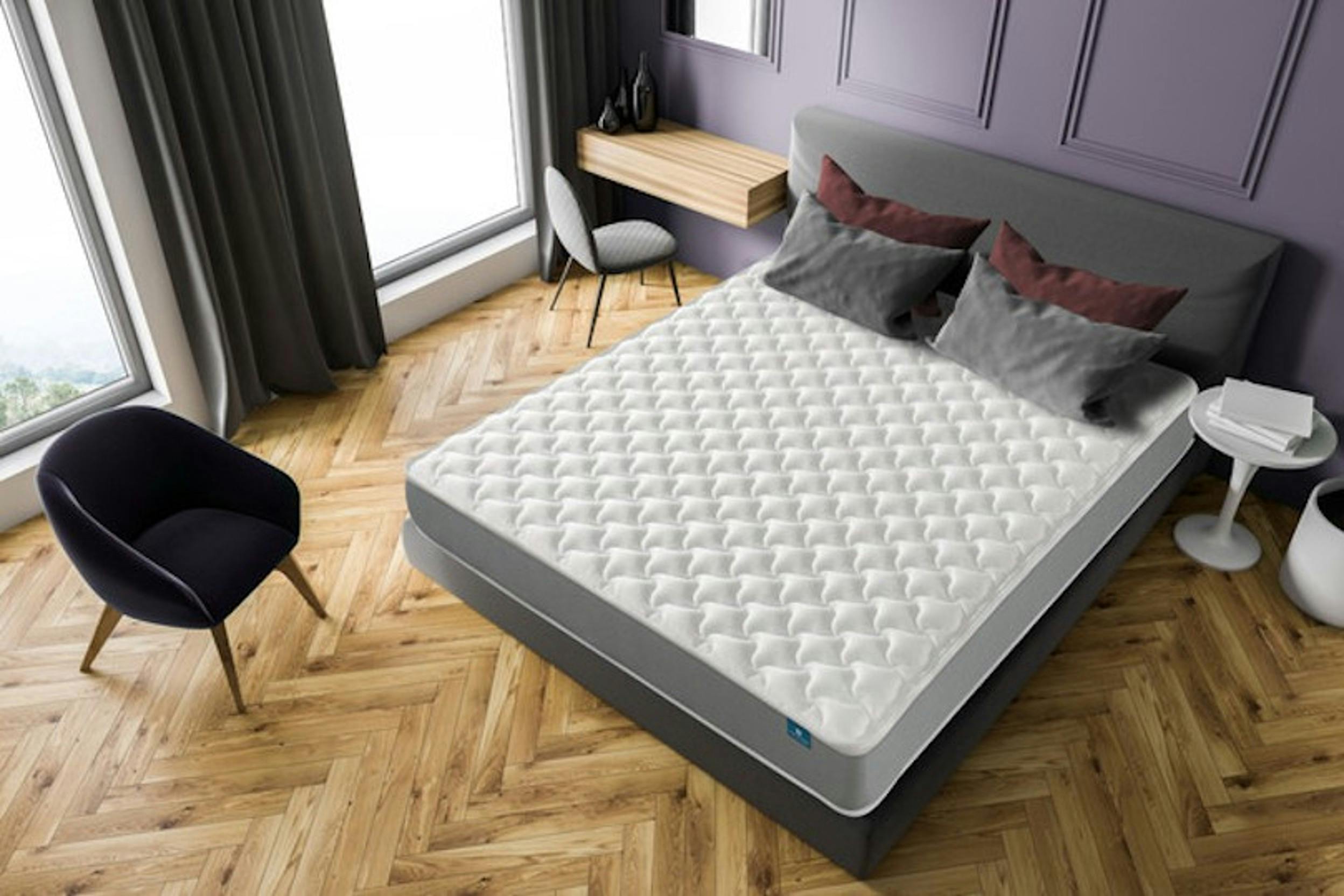 Onopgemaakt bed met gelmatras in een stijlvolle slaapkamer met grijs gestoffeerd bed.
