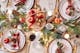 Festlich gedeckter Tisch mit traditioneller Weihnachtsdeo in Rot, Weiß sowie mit Tannengrün, goldenem Geschirr, Lichter- und Kerzenglanz.