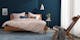 Schlafzimmer in dunkelblauen Nuancen mit Massivholzbett und Stuhl in Flechtoptik