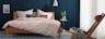 Chambre aux murs bleus nuit avec lit en bois massif, tête de lit et fauteuil en cuir tressé