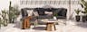 Terrasse im orientalischen Stil mit einem Loungesofa mit grauen Polstern und gemusterten Kissen in Erdtönen, dazu ein kupferfarbener Tisch mit Terrazzo-Platte, ein Sonnenschirm, Kakteen und sonstige Grünpflanzen.
