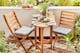 Klein balkon met houten inklapbare meubels, op de kleine tafel staat een bord tomatenmozzarella, brood en wijn; groene planten, grijze zitkussens en een beige outdoor-vloerkleed maken het gezellig.