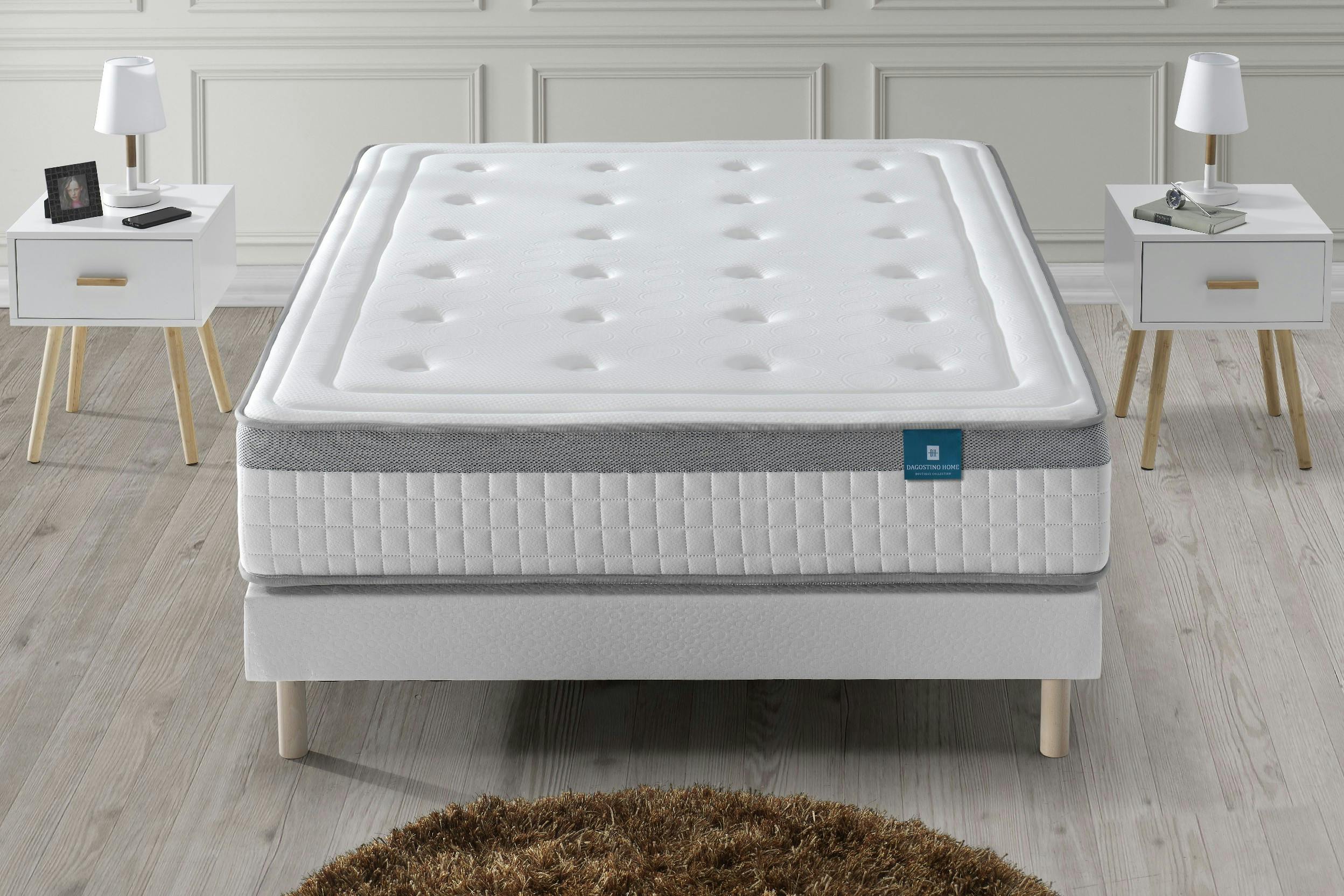 Einfaches Polsterbett mit dicker Gelmatratze, davor ein runder Teppich, links und rechts Nachttische
