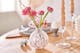 Eine roséfarbene Kugelvase aus Glas mit Blumen auf einem Tisch aus Eichenholz, dazu Kerzenständer mit Twistkerzen.