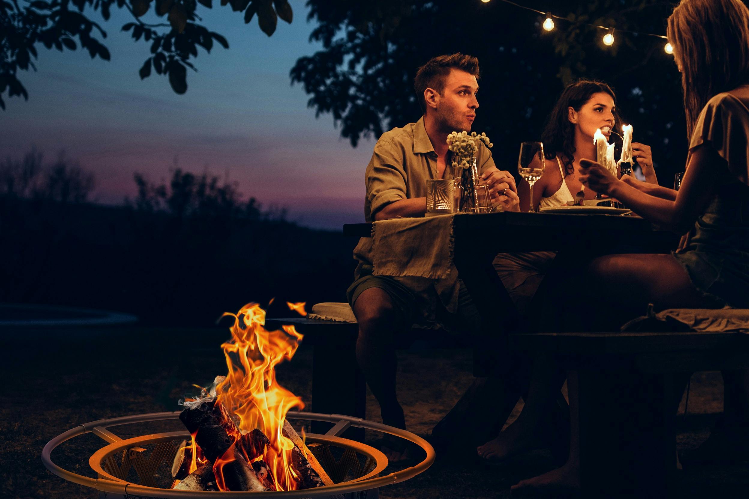Menschen, die ein Abendessen unter freiem Himmel neben einer lodernden Feuerschale genießen