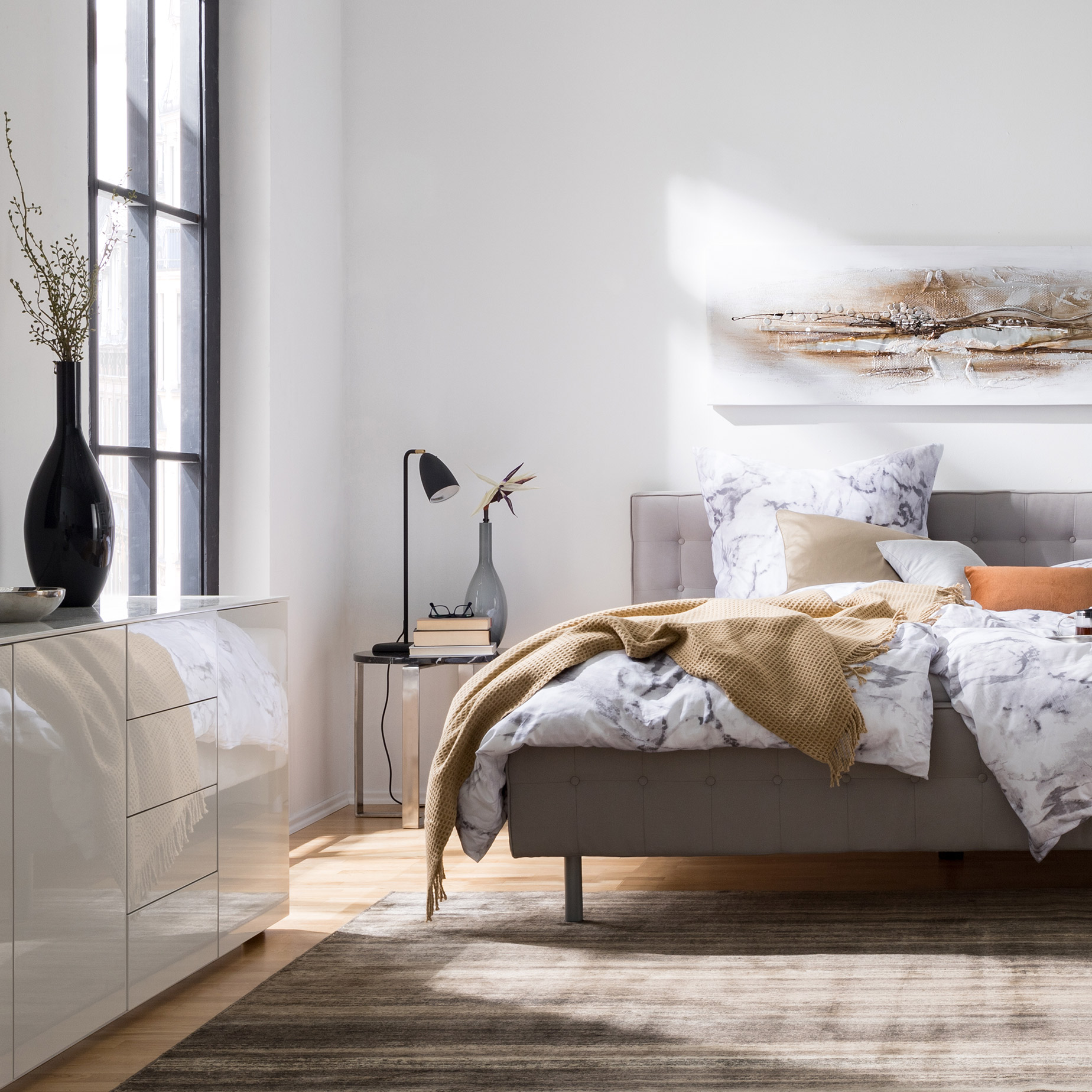 Graues Polsterbett mit weißen Hochglanzmöbeln