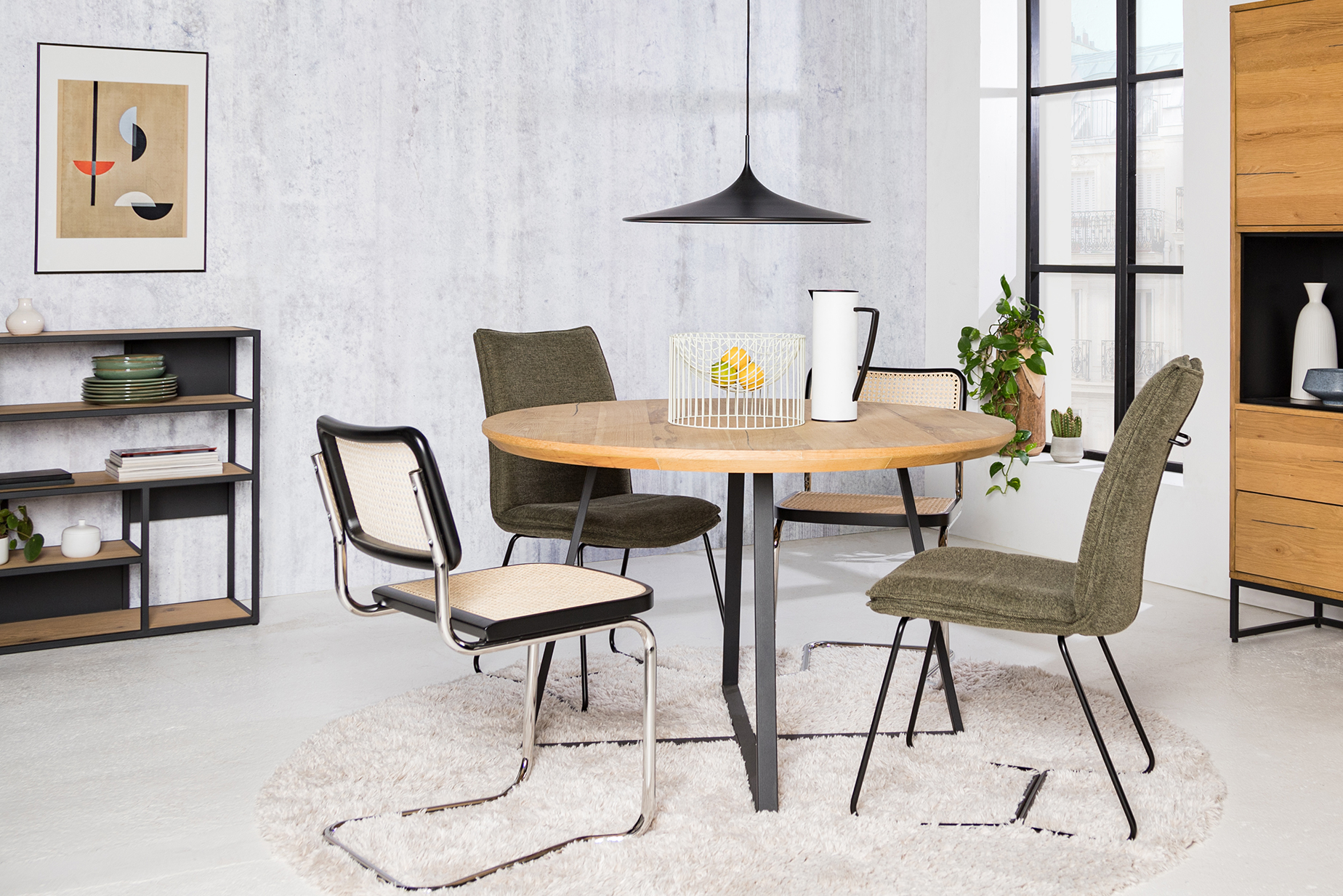 Esszimmer bestehend aus Freischwingern mit Wiener Geflecht und Stühlen aus Chenille-Stoff, dazu Regale im Industrial-Stil, ein weißer Teppich, eine schwarze Pendelleuchte sowie ein Wandbild und Deko.