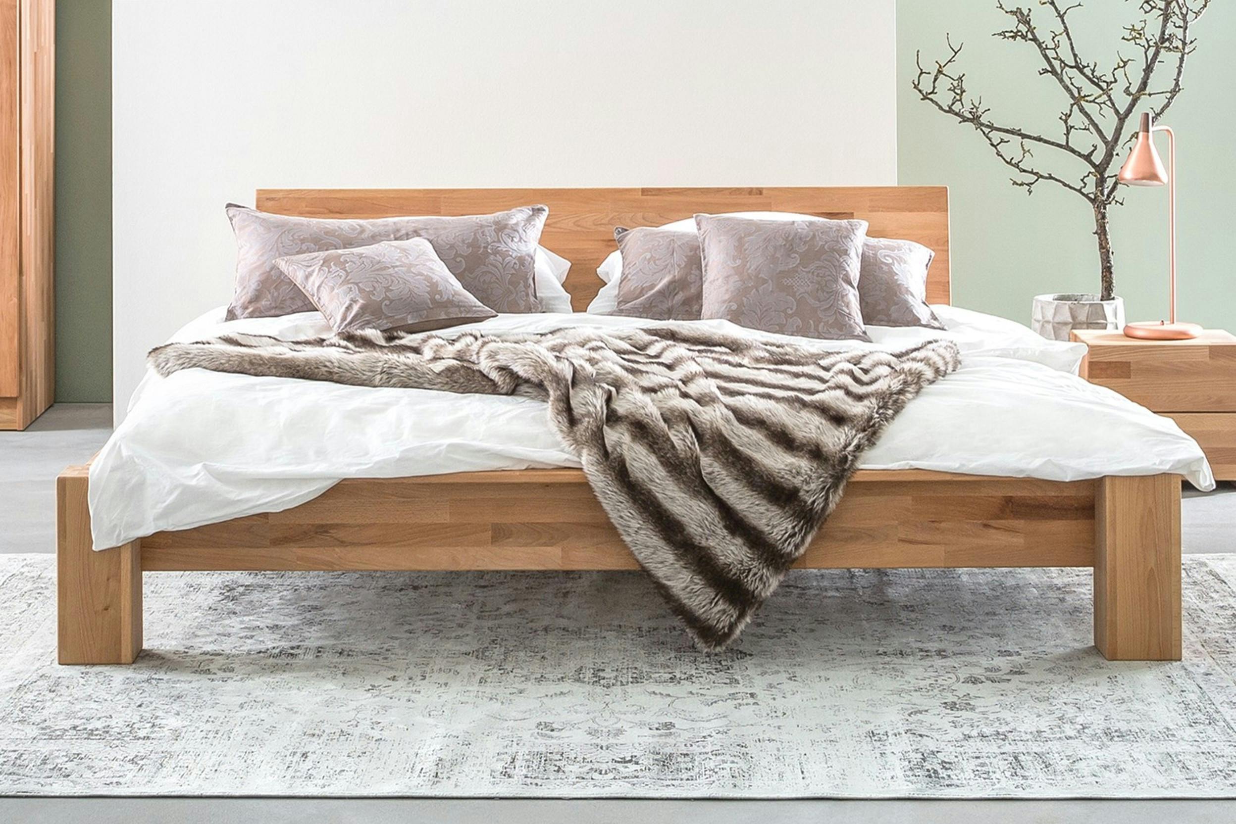 Houten futonbed met hoofdbord van hout, opgemaakt met grijze kussens en wit dekbedovertrek.