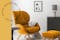 Retro-Sessel aus Samt in Orangegelb mit passendem Hocker auf einem schwarz-weißen Teppich, dazu ein schwarzer Beistelltisch, ein mattgraues Sideboard, ein Deko-Spiegel, eine Tischleuchte aus Beton sowie ein Wandbild mit Audrey Hepburn; daneben eine schwarze Pendelleuchte aus Metall.