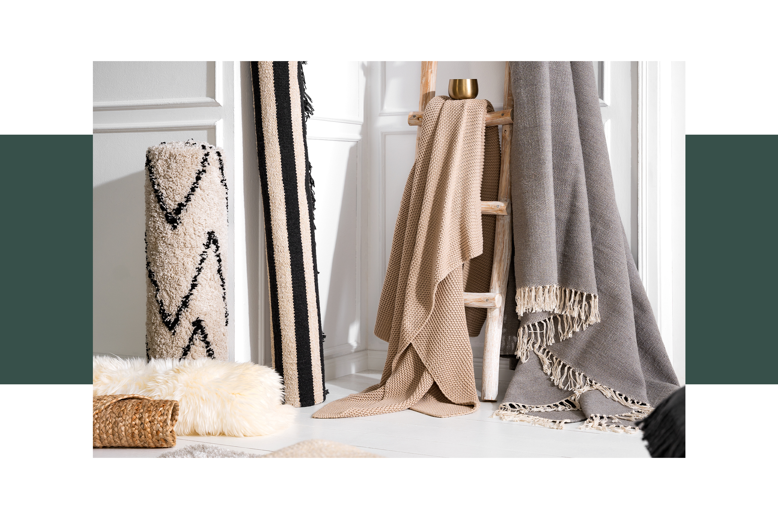 Textilien wie Teppiche und Decken aus verschiedenen kuschelig-flauschen Materialien wie Wolle, Faux-Fur, Grobstrick und Fransen für eine gemütliche Winterzeit, daneben weihnachtliche Dekoration auf einem Schafsfell.