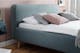 Blauw gestoffeerd bed met kussens tegen roze wand