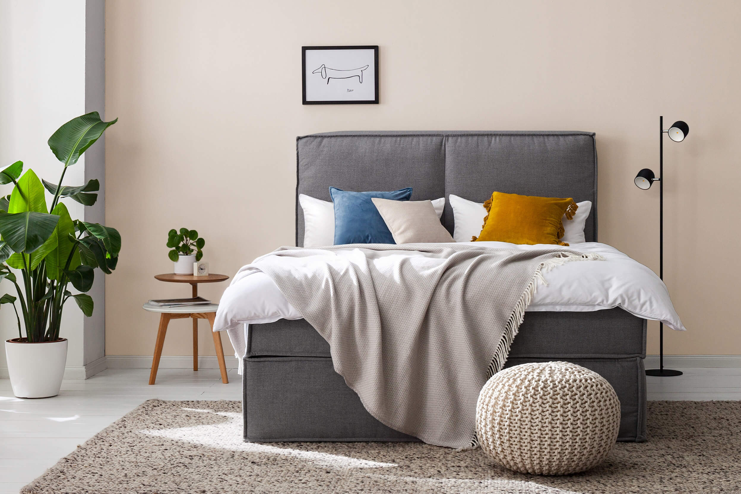 Dunkelgraues Boxspringbett mit farbigen Kissen vor beigefarbener Wand