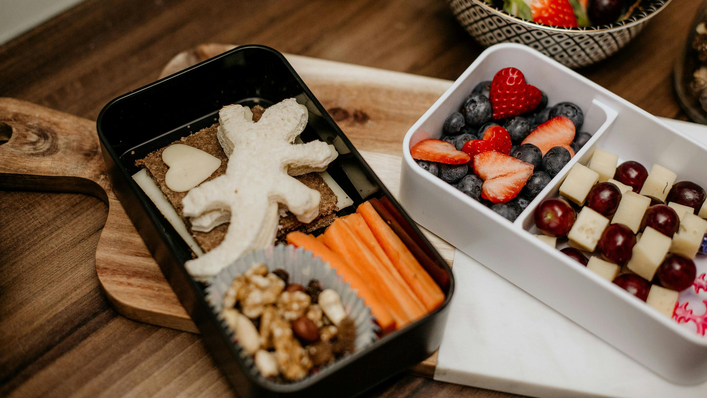 Lunchboxen in Schwarz und Weiß, mit Gemüse und Obst beüfüllt, auf Arbeitsbrett aus Massivholz (Marke: Butlers).