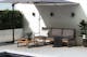 Auf einer hellen Terrasse steht eine Outdoor-Lounge aus modularen Gartenmöbeln im Industrial-Look mit dunklen Stahlbeinen, Sitzflächen aus Akazienholz und dunklen Sitzpolstern