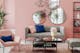 Salon dans les tons rose pastel, avec plusieurs miroirs sur le mur, des meubles gris clair et rose, et une déco minimaliste comme une plante, une table et quelques étagères.