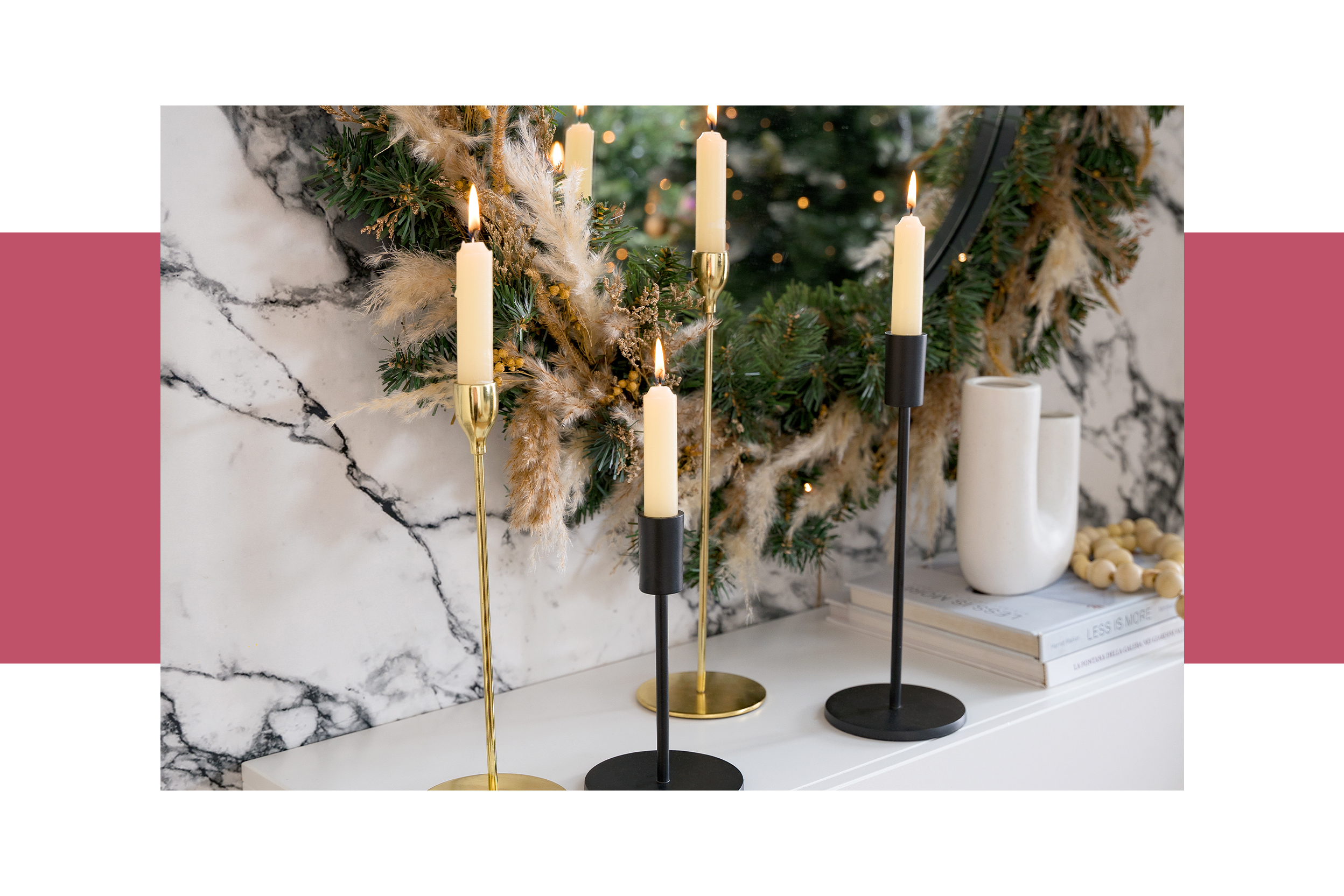 Weiße Kerzen in goldenen und schwarzen Kerzenhaltern vor einem Weihnachtskranz an einer Marmorwand; daneben bunte gedrehte sowie glatte Kerzen.