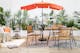 Terrasse de style bohème avec chaise suspendue, photophores en bambou, tapis d'extérieur noir et blanc et parasol orange, le tout accompagné de coussins et de plaids, de nombreuses plantes vertes et de meubles de jardin en acacia et en métal.