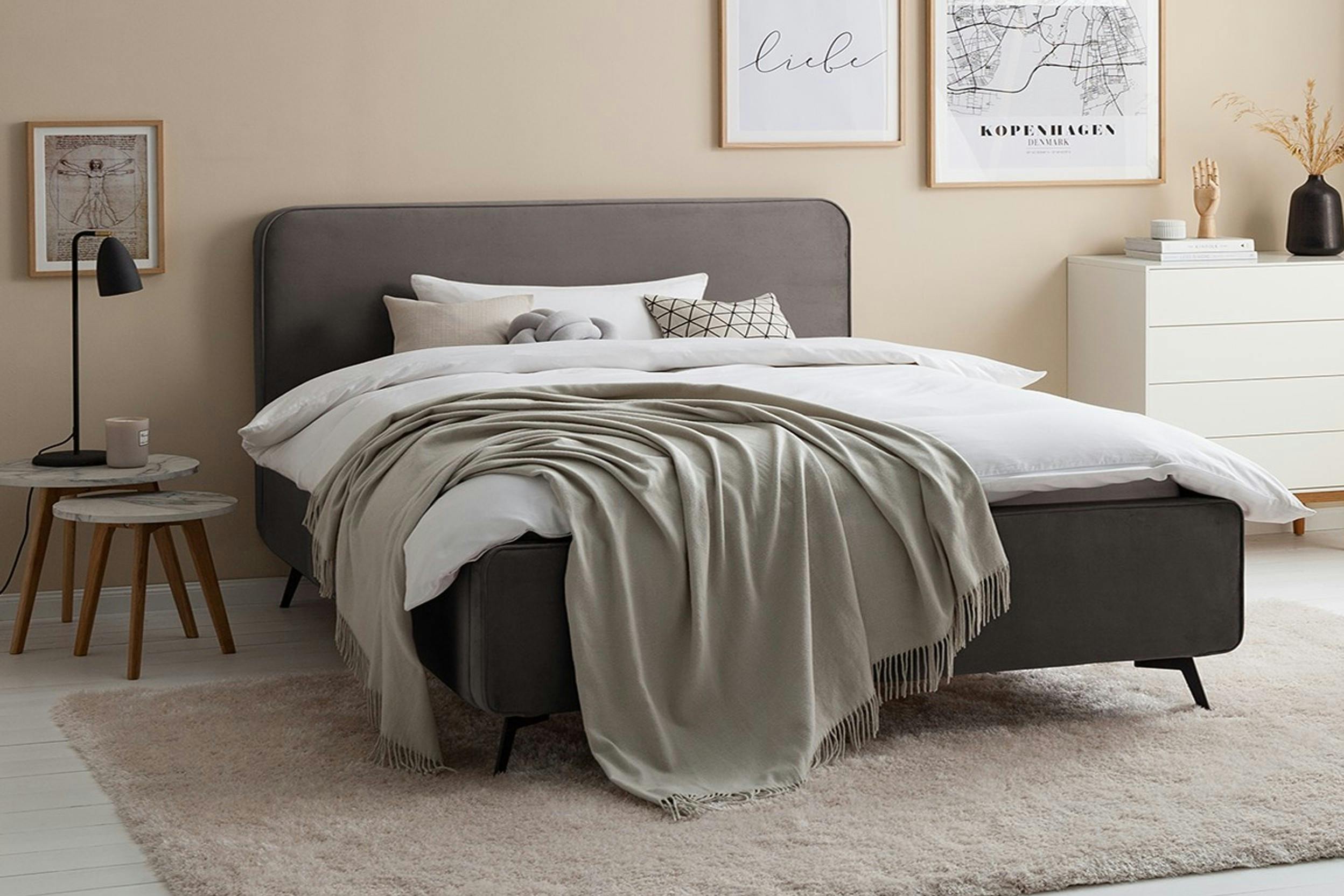 Graues Polsterbett mit weißer Bettwäsche in einem neutral eingerichtetem Schlafzimmer