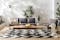 Terrazzo con divani modulari e tavolino in legno e metallo, cuscini antracite, plaid bianco crema e cuscino bianco con motivi geometrici su tappeto in bianco e nero.