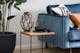 Beistelltisch aus Holz mit Metallbeinen neben blau bezogenem Sofa und Pflanze in schwarzem Blumentopf