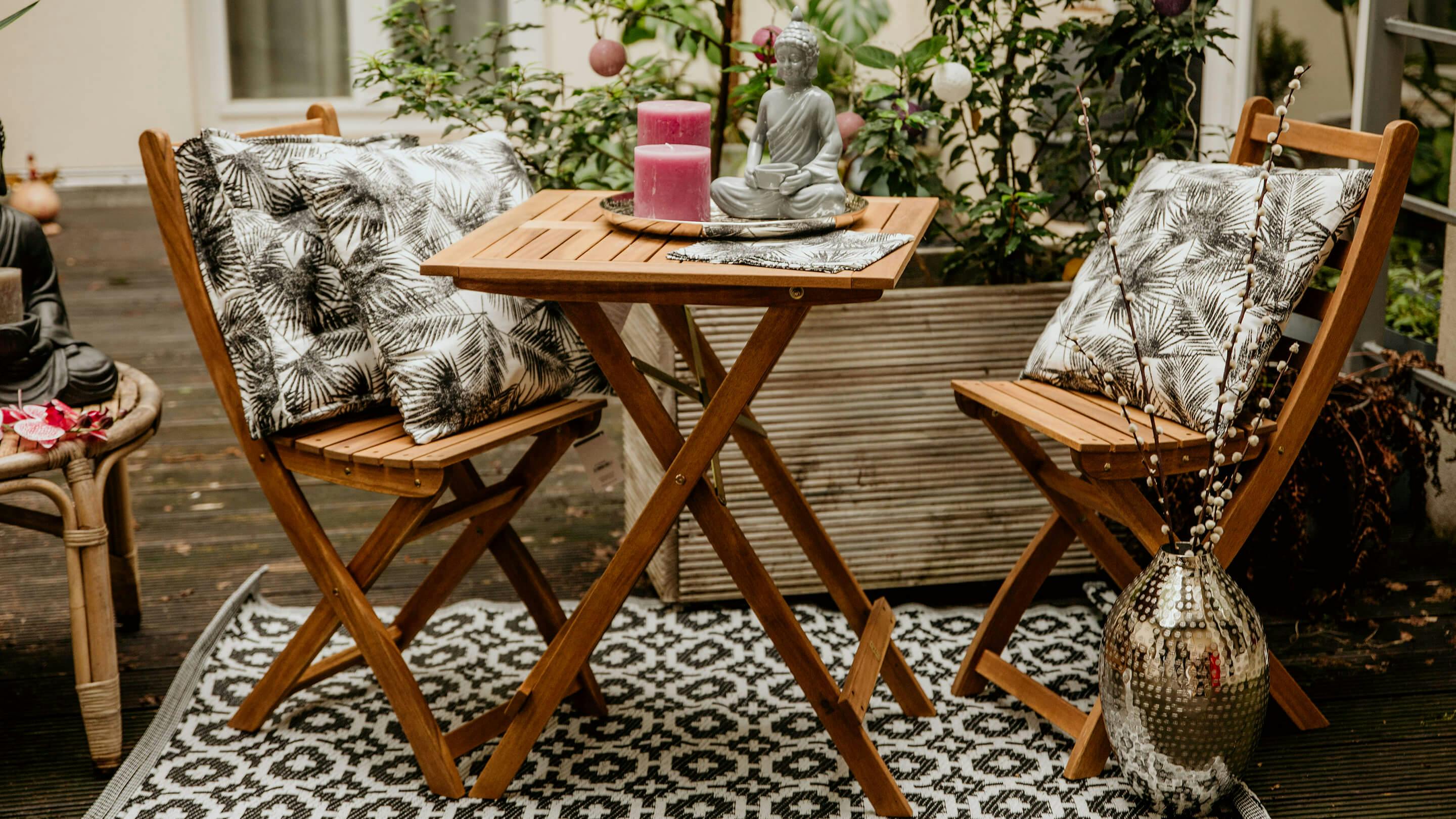 Terrasse mit kleinem Gartentisch-Set aus Massivholz, Outdoor-Teppich in Schwarz u. Weiss, Kissen und Deko-Objekten (Butlers).