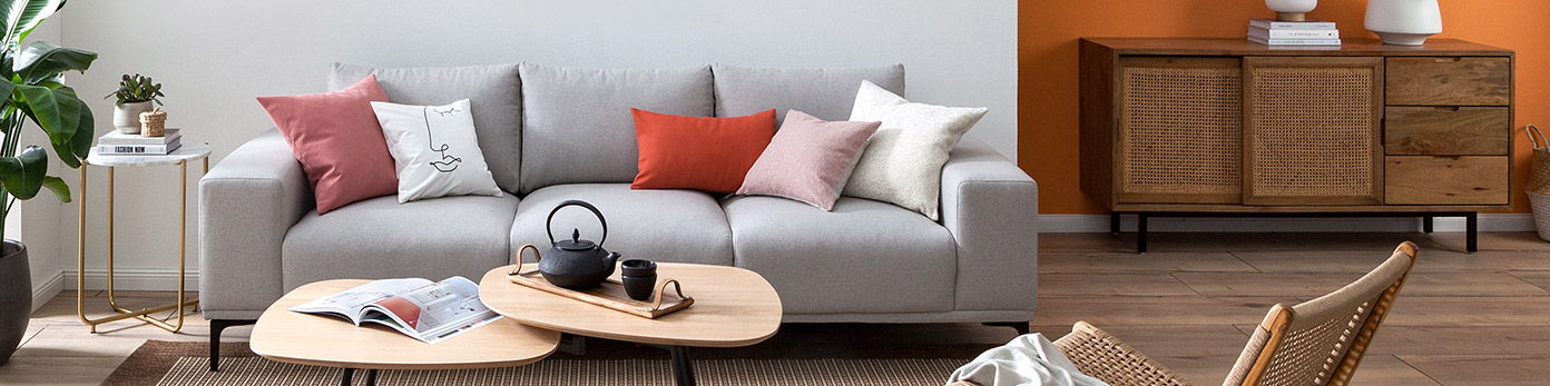 Hellgraues Sofa mit Kissen in Rosa- und Rottönen und weitere Wohnzimmermöbel aus Holz