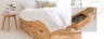 Lit en bois clair avec 3 tiroirs de rangement, linge de lit blanc et suspensions blanches au-dessus de la table de nuit en filigrane.