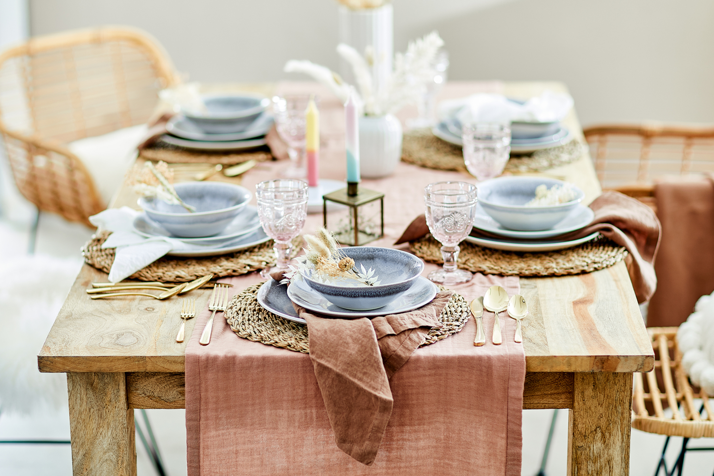 Gedeckter Brunchtisch, Esszimmermöbel aus natürlichem Echtholz und Rattangeflecht, Tafel eingedeckt mit Keramikgeschirr, rosa Glaskelchen, Goldbesteck auf einem Tischläufer aus Baumwollmusselin.