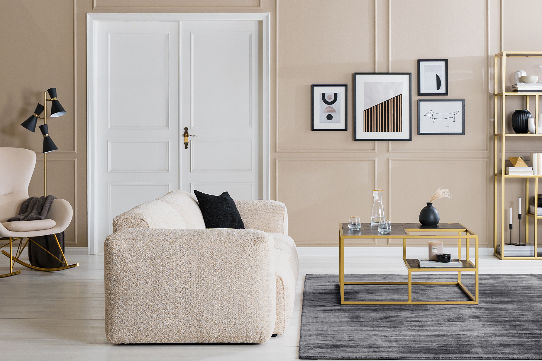 Wohnzimmer mit einem beigen Bouclésofa und -sessel; ein Couchtisch, Regal, TV-Board sowie eine Kommode in einer eleganten Schwarz-Gold-Kombination, dazu schwarze und weiße Deko und viele Textilien.