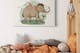 Lit d'enfant en bois clair, avec du linge de lit dans des tons ocres, des peluches gris clair et un tableau avec un dessin d'éléphant sur le mur ; dans l'image en vignette, deux pots BUTLERS avec couvercles en bois et imprimés d'animaux mignons dessinés dessus.