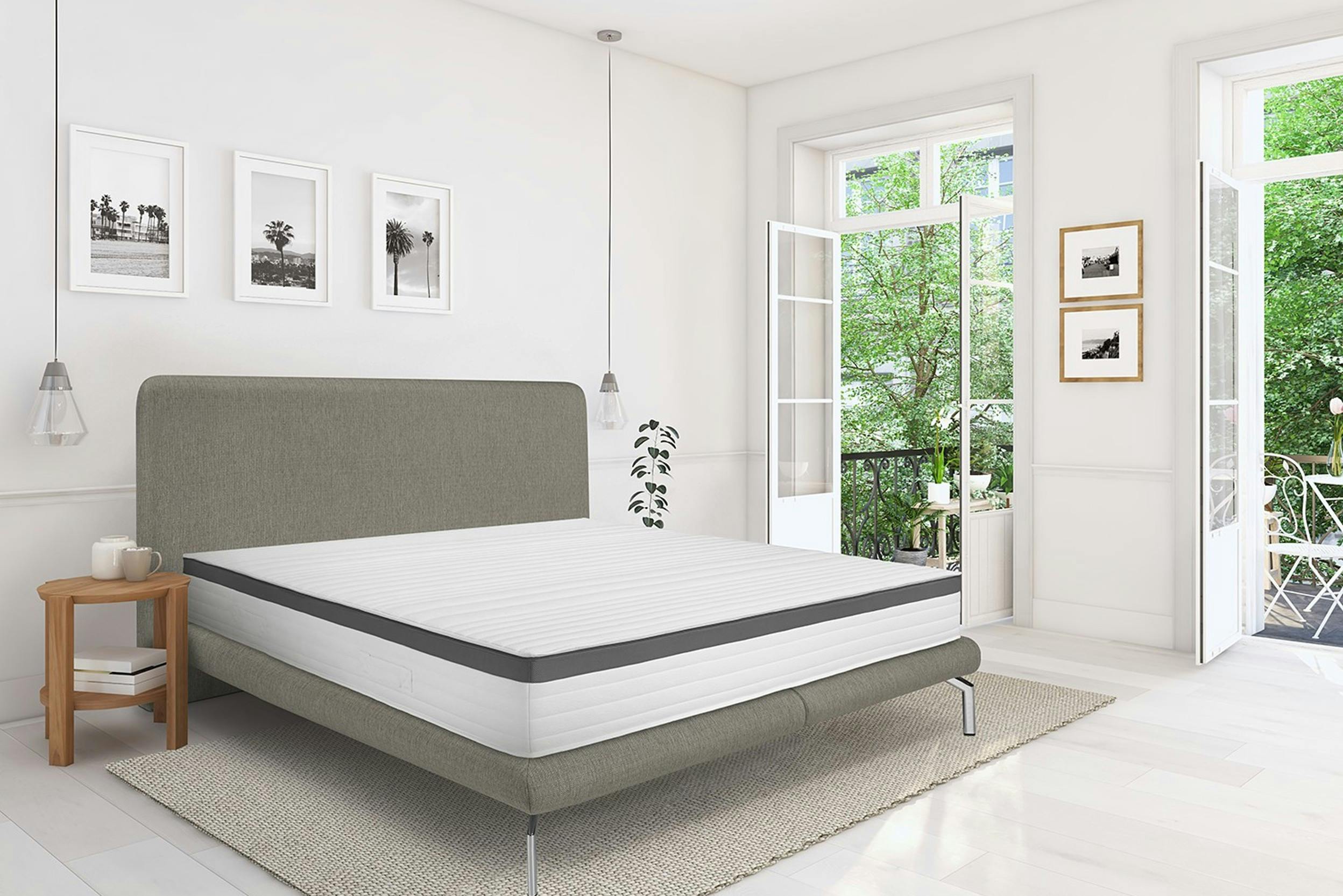 Helles Zimmer mit weit geöffneten Fenstern und grauem Bett samt Matratze