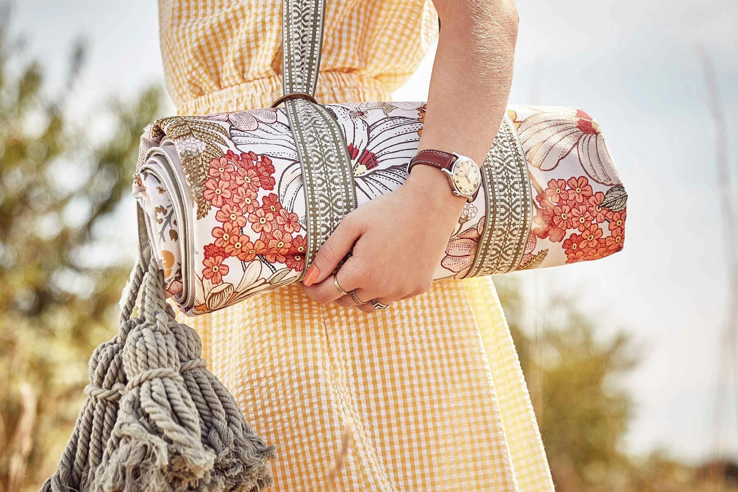 Frau in einem karierten Sommerkleid mit einer mit Blumen und Quasten verzierten Decke unter dem Arm