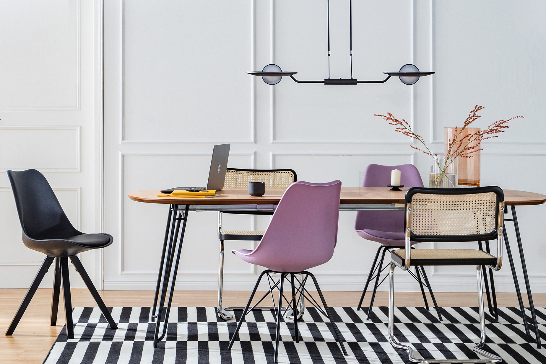 Esszimmer mit Esstisch und Stühlen in Schwarz, Lila und mit Wiener Geflecht auf schwarz-weißem Teppich, dazu eine Pendelleuchte mit Glas sowie ein schwarzes Leiterregal.