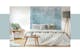 Camera da letto con tavolini in legno chiaro e lampada in stile scandinavo, abbinati a un letto con lenzuola bianche e cuscini grigio chiaro, sullo sfondo un fotomurale blu ghiaccio