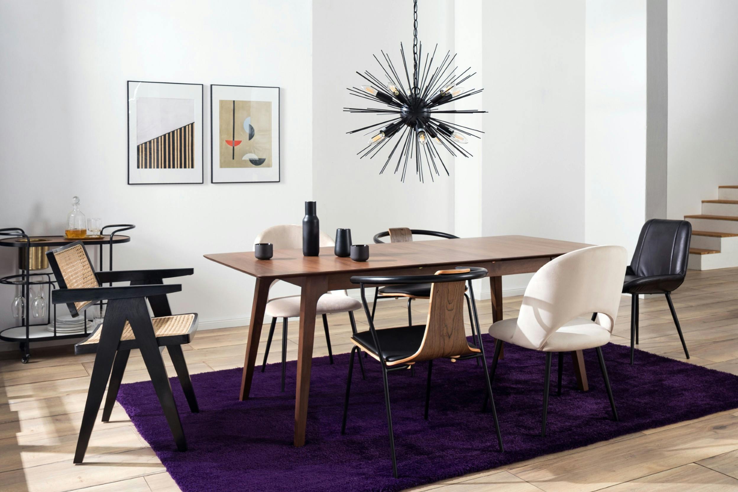 Eklektisch angehauchtes Esszimmer mit Holztisch, lila Teppich und verschiedenen Stühlen und schwarzer Pendelleuchte
