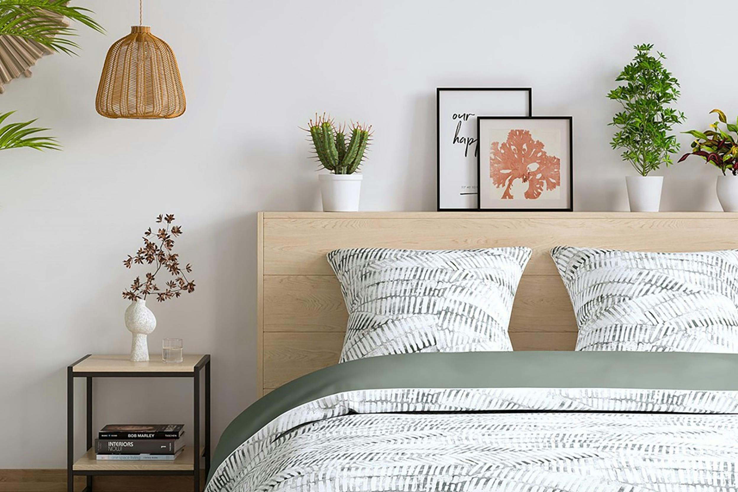 Gemusterte Bettwäsche in Salbeigrün auf einem mit Bildern und Pflanzen dekoriertem Holzbett