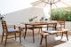 Terrasse mit Gartentisch, Gartenstühlen und Gartenbank aus Akazienholz mit hellblauen Sitzkissen, dazu ein weißer Sonnenschirm, ein gemusterter Outdoor-Teppich und Deko.