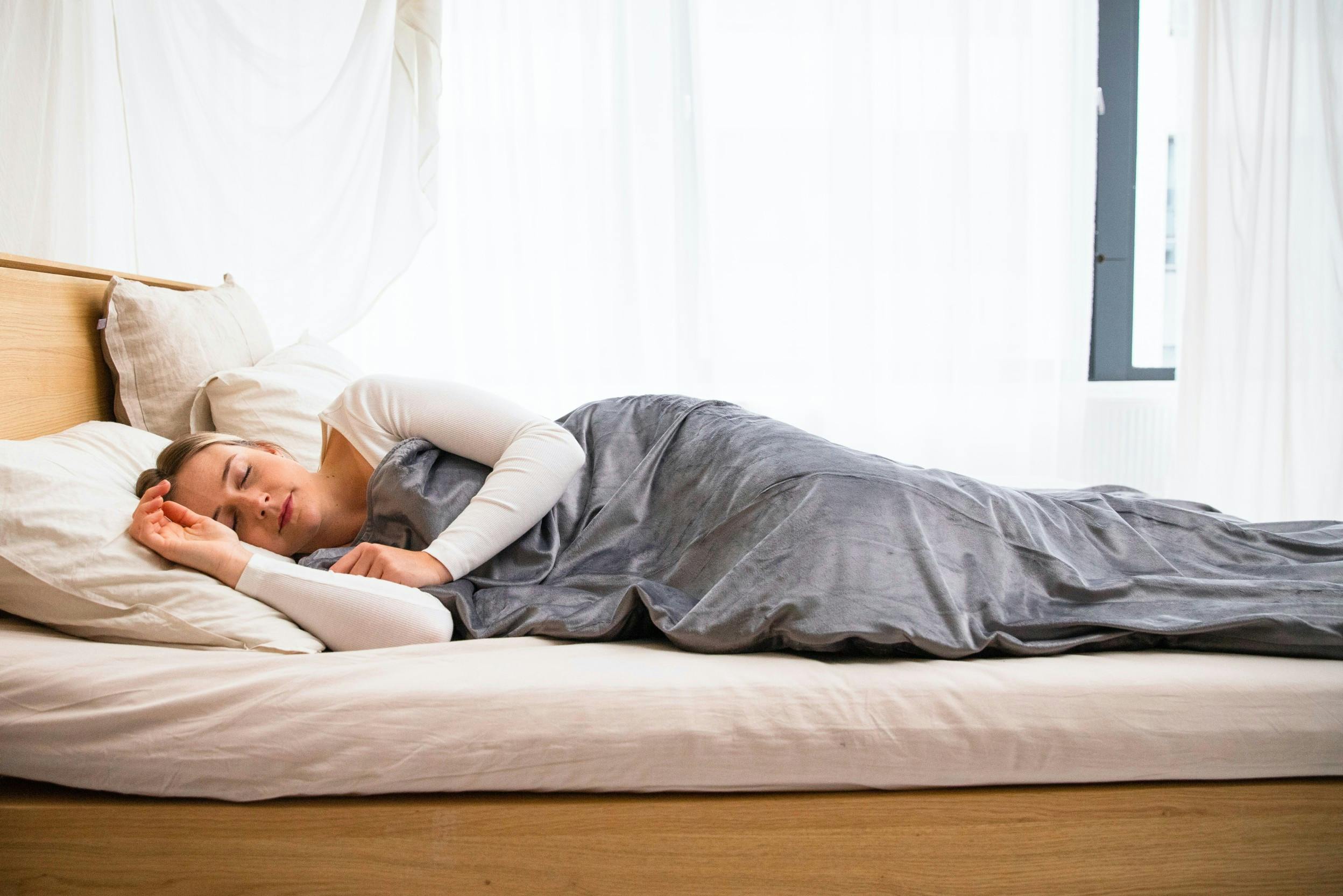 Seitlich schlafende Frau mit grauer Kuscheldecke auf einem Holzbett