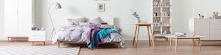 Schlafzimmer mit Futonbett mit grauer Bettwäsche sowie Wandschränke, Regale und zwei Beistelltische