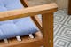 Gartenstuhl aus Akazienholz mit hellblauem Sitzkissen auf einem grau-weißen Outdoor-Teppich mit Rautenmuster.