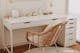 Simpel en doeltreffend ingerichte thuiswerkplek met een wit bureau en rotan stoel in boho-stijl en overdadige goudkleurige woonaccessoires voor een glamoureuze look en een witte, geometrische wandafbeelding.