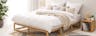 Holzbett mit offenem Bettgestellt, weißer Smood-Matratze, beigen Schlafzimmertextilien und einem Würfelregal als Nachttisch