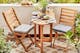 Klein balkon met houten inklapbare meubels, op de kleine tafel staat een bord tomatenmozzarella, brood en wijn; groene planten, grijze zitkussens en een beige outdoor-vloerkleed maken het gezellig.