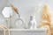 Weiße Keramikvasen in trendiger Kreis- und Po-Form sowie filigrane goldene Kerzenständer und Wandspiegel in weißer Umgebung